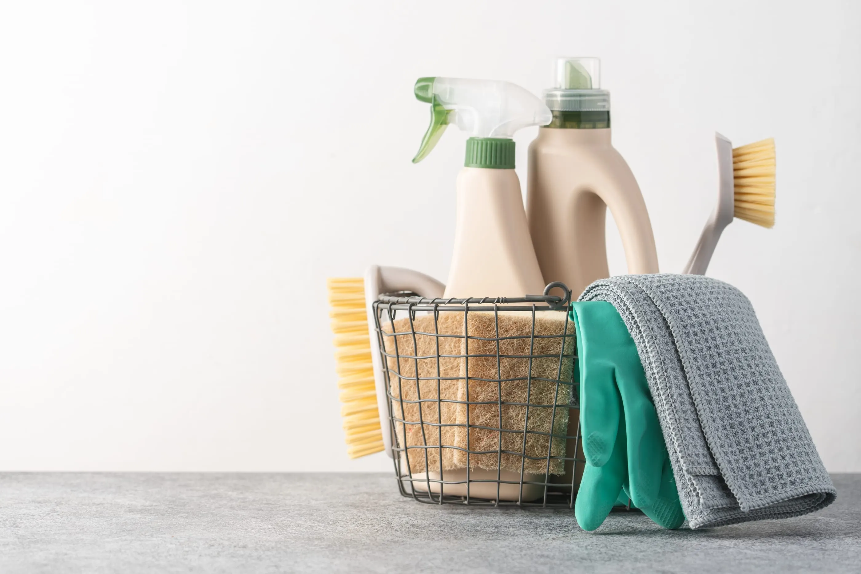 A basket of cleaning supplies: spray bottle, detergent, brushes, sponges, gloves and a microfibre cloth.