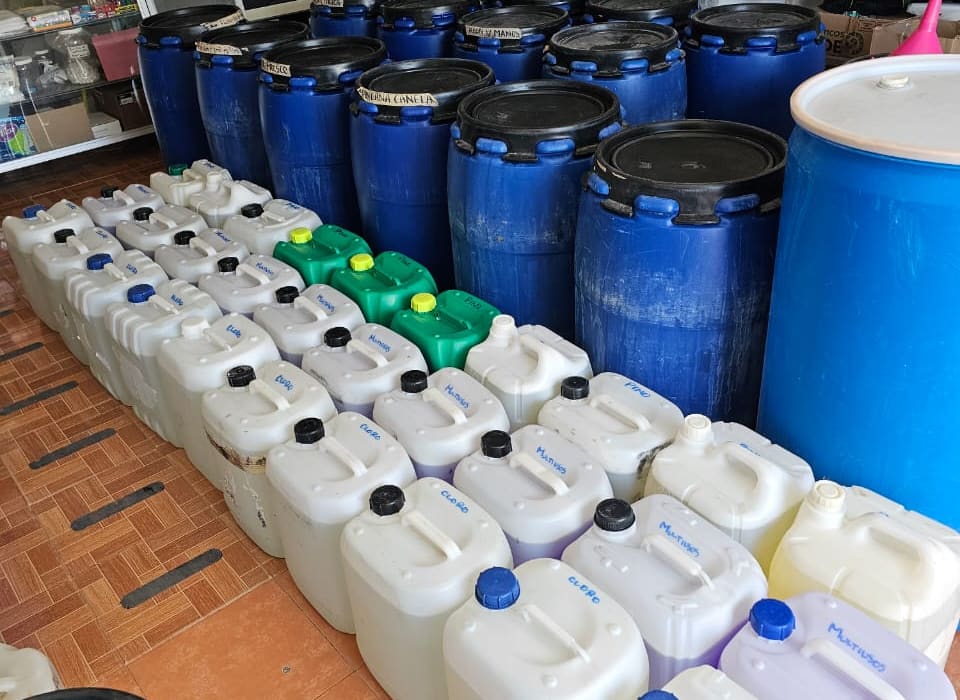 Rows of 20-litre containers hand-labelled bleach, multipurpose and pine, next to blue drums on the shop floor in San José del Cabo.